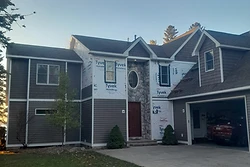 Two-story house under construction with grey siding, stone entry, and Tyvek wrap by All Aspects