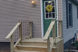 New pressure-treated wood staircase with black wire railings leading to a side door by All Aspects