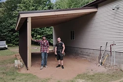 Newly built carport with dark brown metal roof and natural wood beams attached to a house by All Aspects