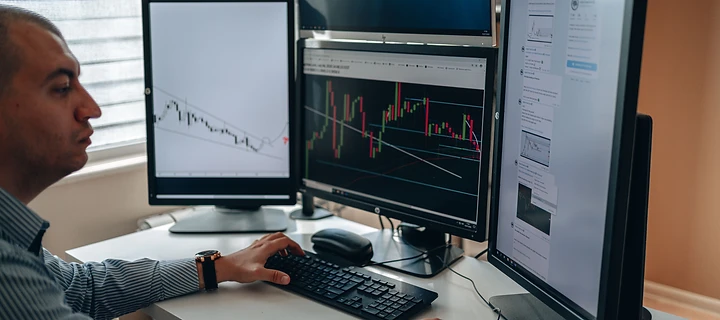 Trader at a multi-monitor workstation reviewing markets