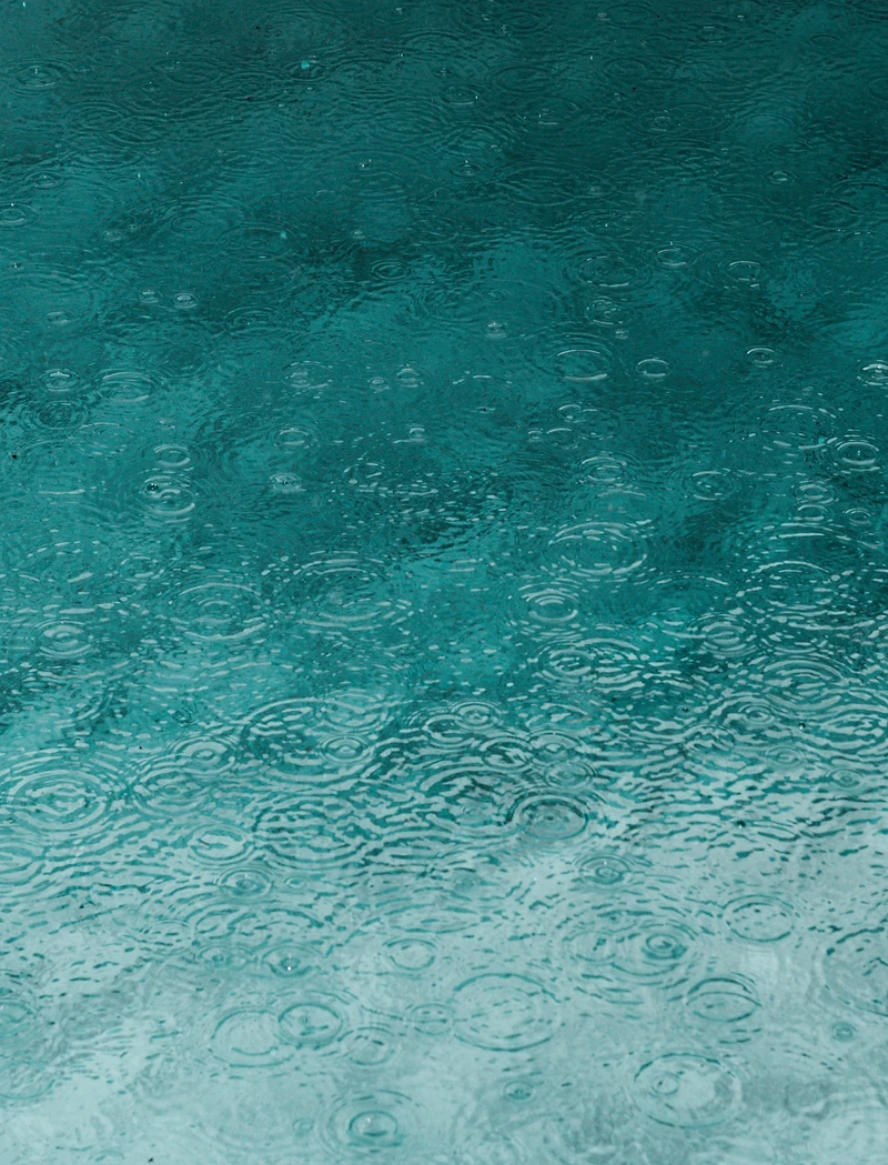 Rain ripples on teal water surface