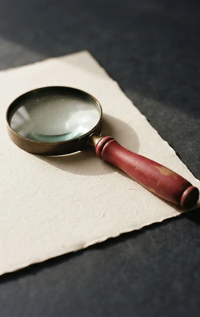 A red magnifying glass resting on a sheet of cream paper