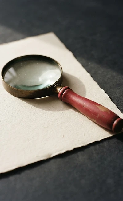 A red magnifying glass resting on a sheet of cream paper