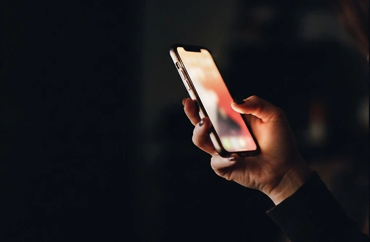A hand reading a glowing phone at night