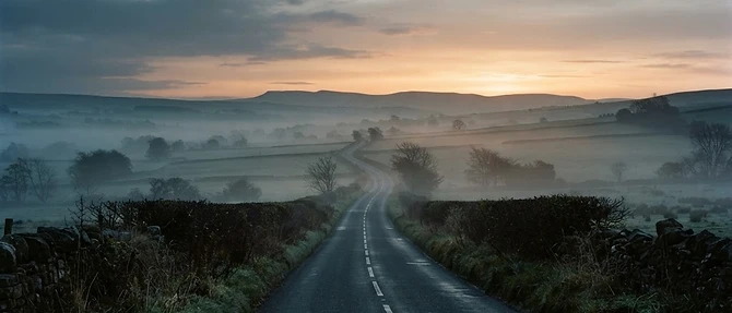 An empty country road running to the horizon at dawn under a band of amber light