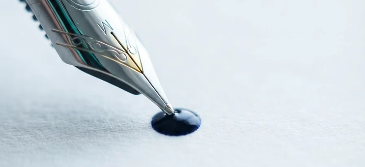 Macro detail of a fountain pen nib meeting paper with navy ink