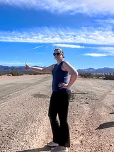Person giving a thumbs-up while standing on a desert dirt road under a bright blue sky