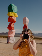 Person holding a camera in front of colorful stacked-rock sculptures at 7 Magic Mountains, Nevada