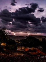 Desert night scene under a stormy sky with lightning behind silhouetted mountains in Sedona, Arizona