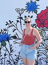 Person smiling in front of a colorful floral mural on a white cinder block wall in New Tazewell, Tennessee