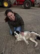 Woman kneeling on concrete petting a black-and-white dog on its back at a rural farm
