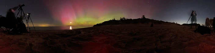 Aurora pillars over a dark beach with photographers at tripods