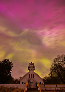 A white lighthouse under a vivid magenta and green aurora sky