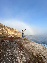 Person with arms outstretched on a coastal cliff at Big Sur, California