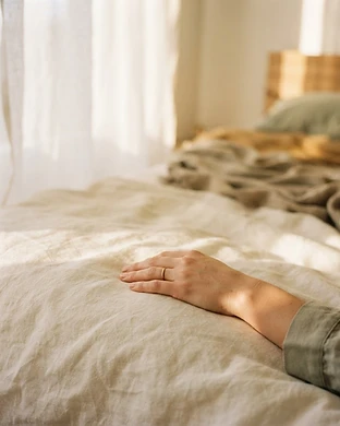 A woman's hand resting gently on a soft linen sheet in warm morning light