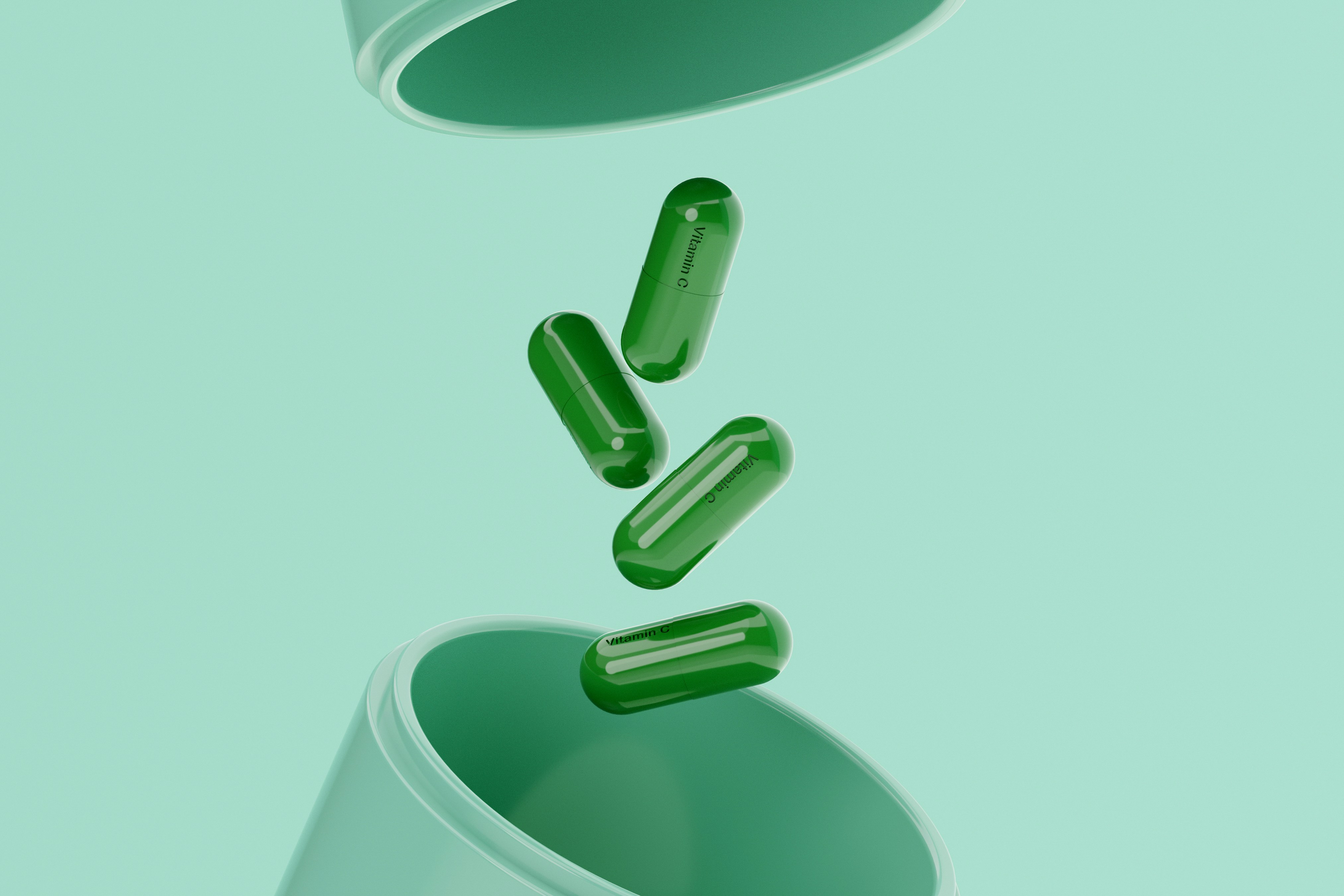 Four dark green capsules printed with Vitamin C text floating between the open top and bottom halves of a larger green capsule container against a flat mint green background