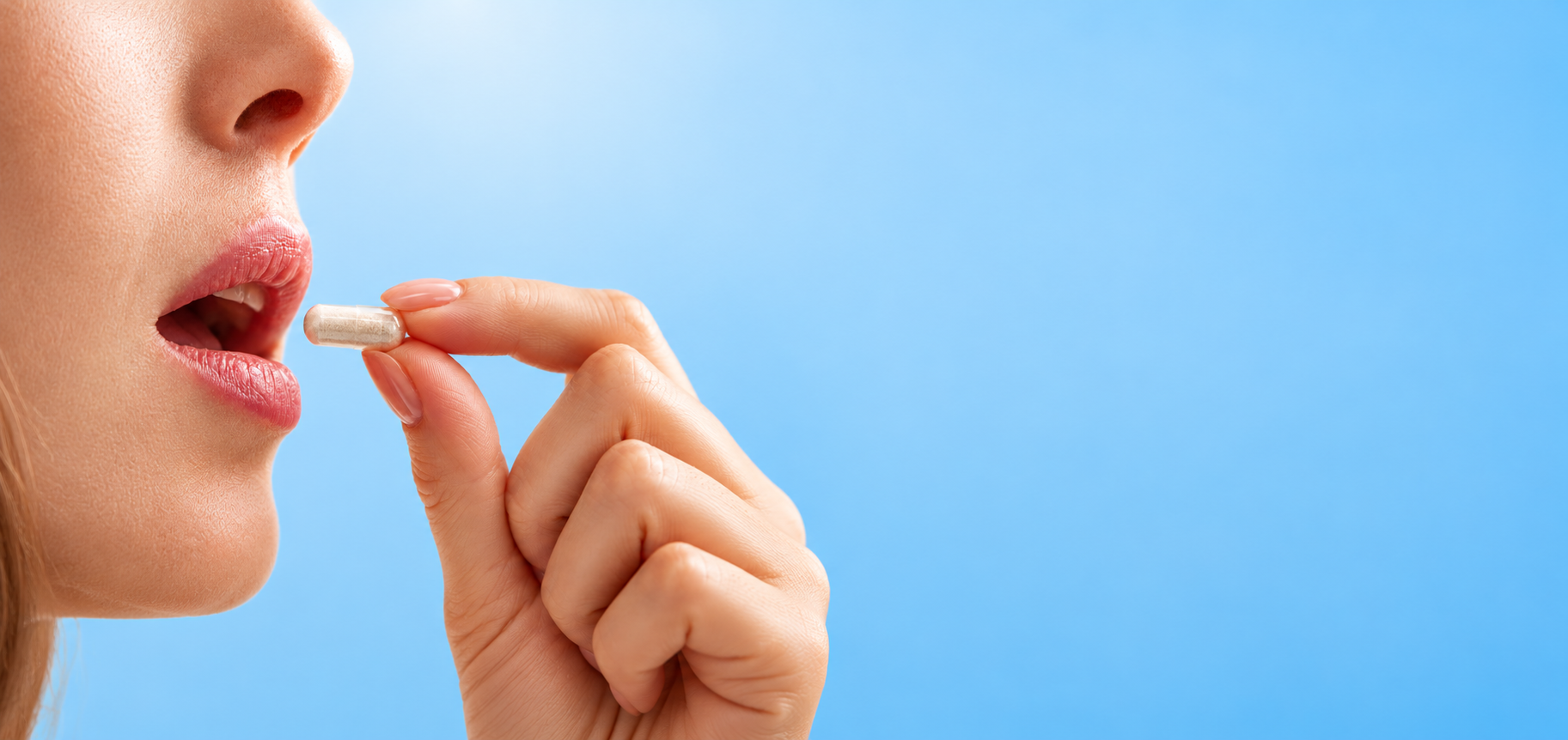 Woman holding a transparent powder-filled capsule near her lips, on a light blue background