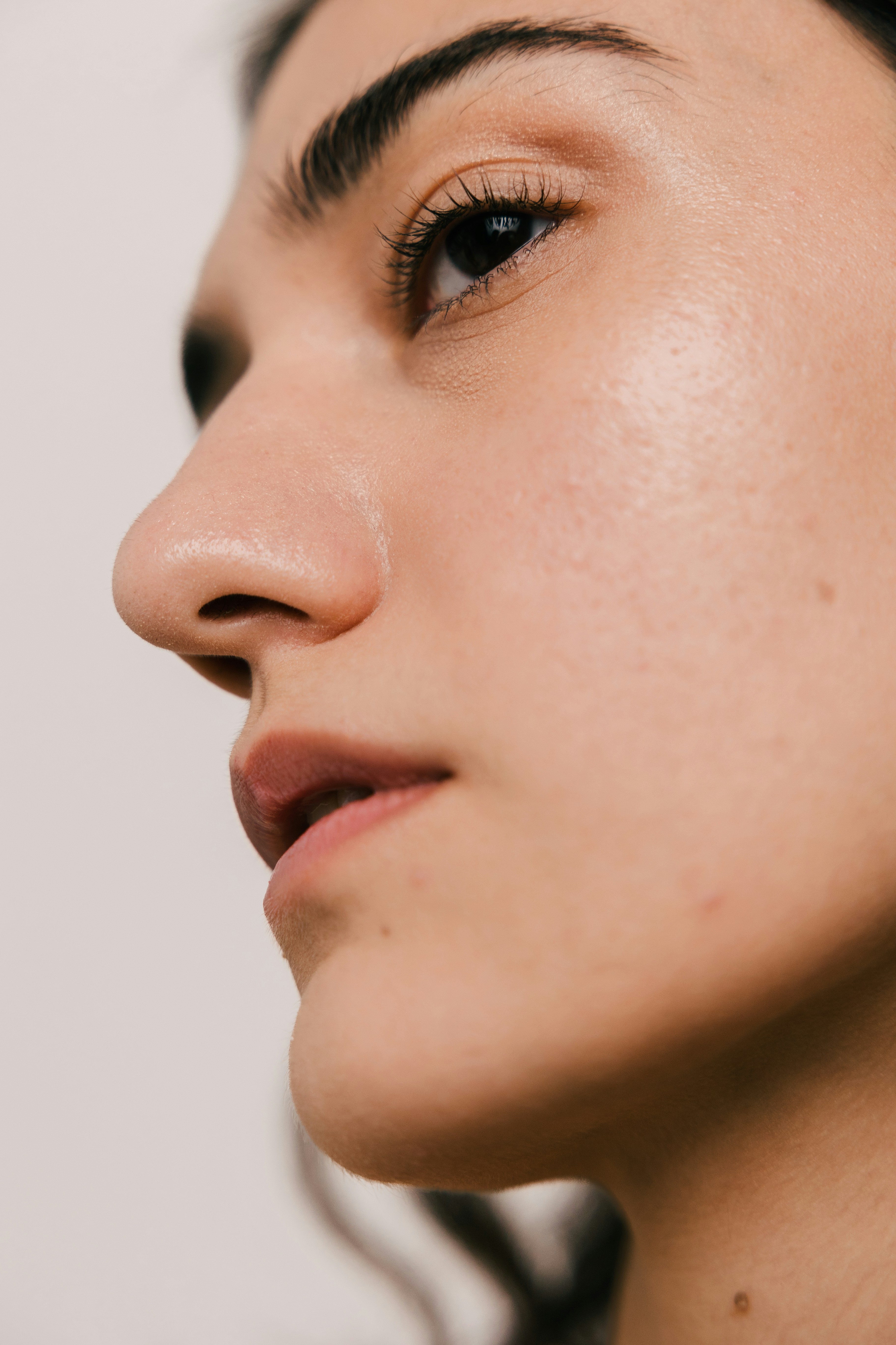 A close-up profile of a woman's face showing natural skin texture, dark hair and eyebrows, lips slightly parted, in soft natural light