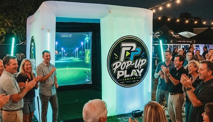 Guests cheering around a glowing golf simulator at an event