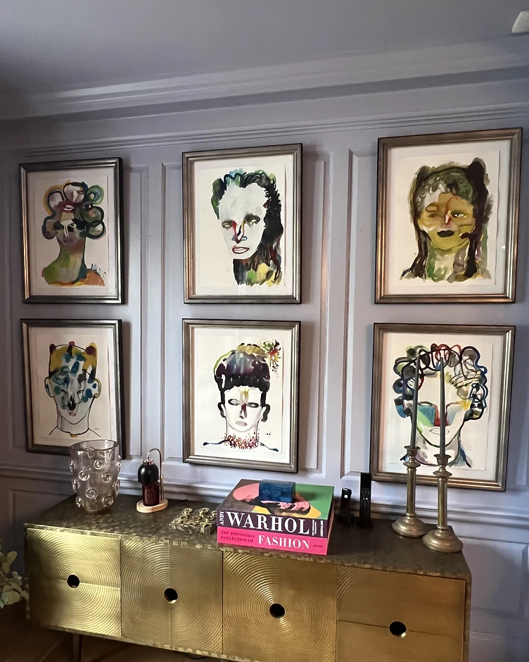 A symmetrical gallery wall of six custom-framed watercolor portraits above a brass mid-century sideboard
