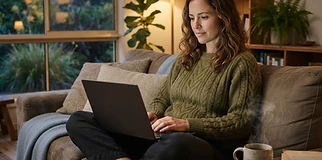 Relaxed person on a couch with a laptop and a cup of tea, soft evening light