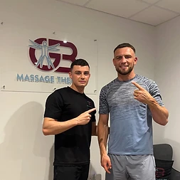 George with a client pointing to the GB Massage Therapy sign at the Fort Dunlop clinic