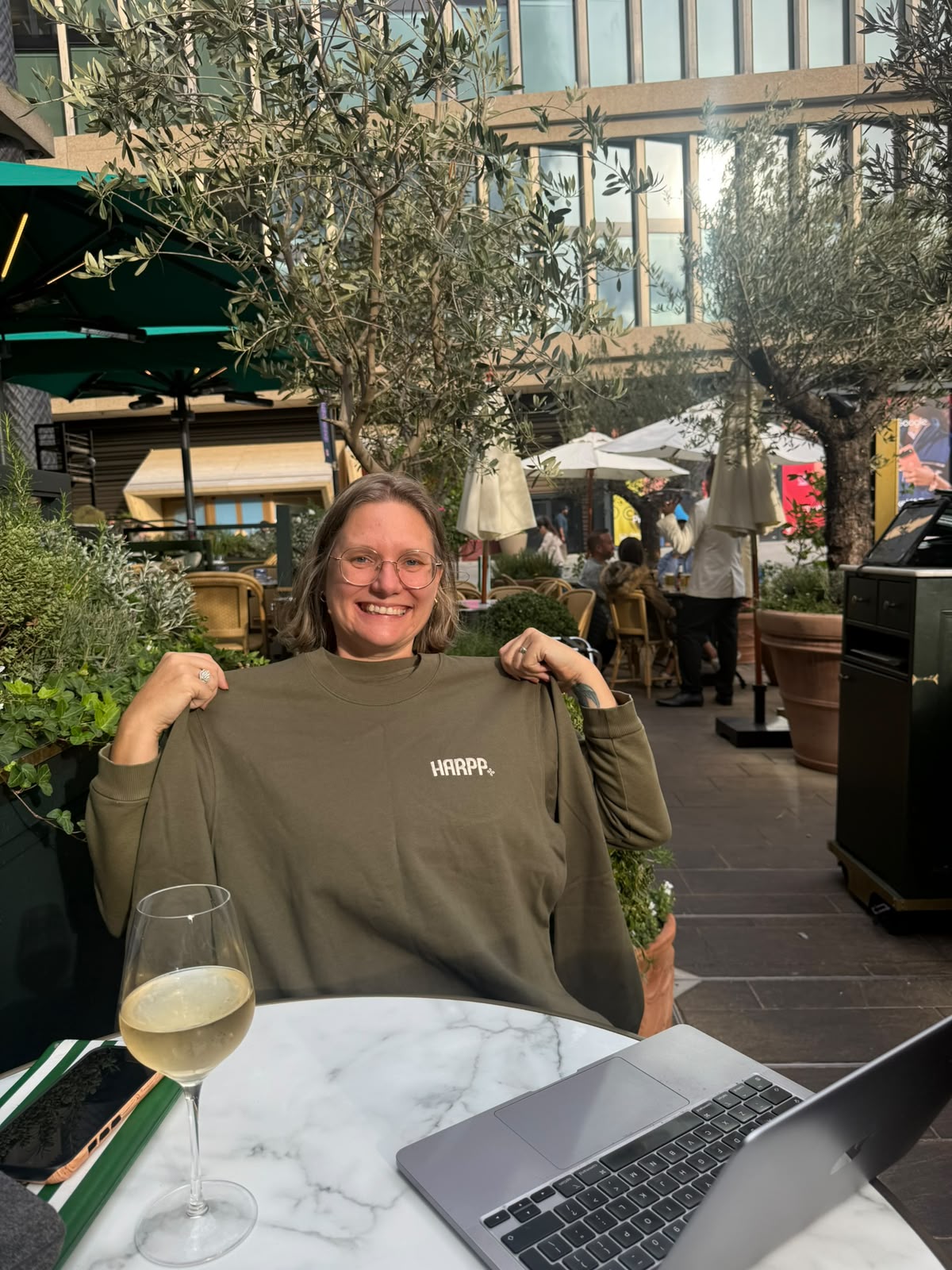 A member of the team holding up an olive HARPP+ sweatshirt at an outdoor table