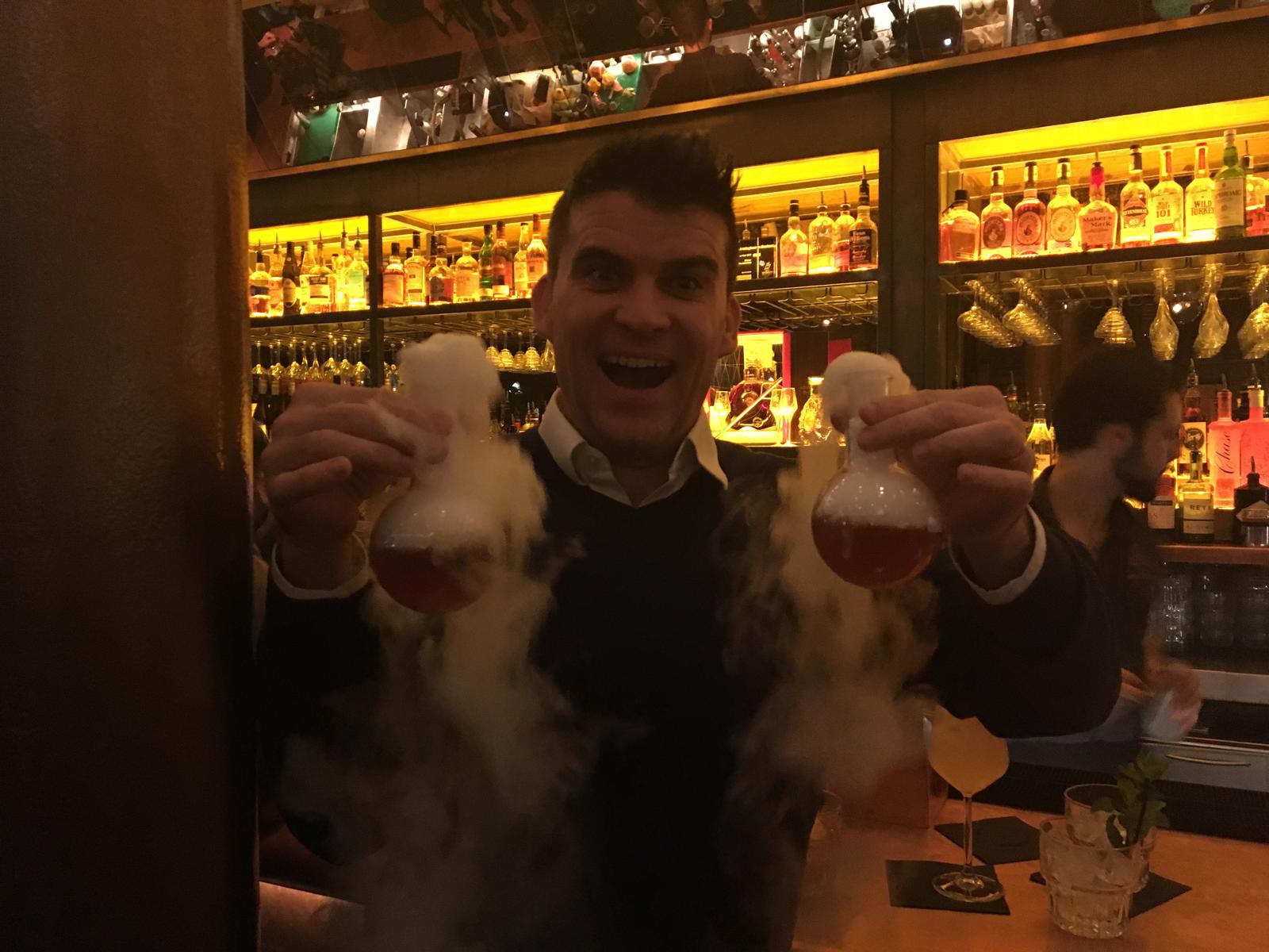 A member of the team holding two dry-ice cocktail flasks at a bar