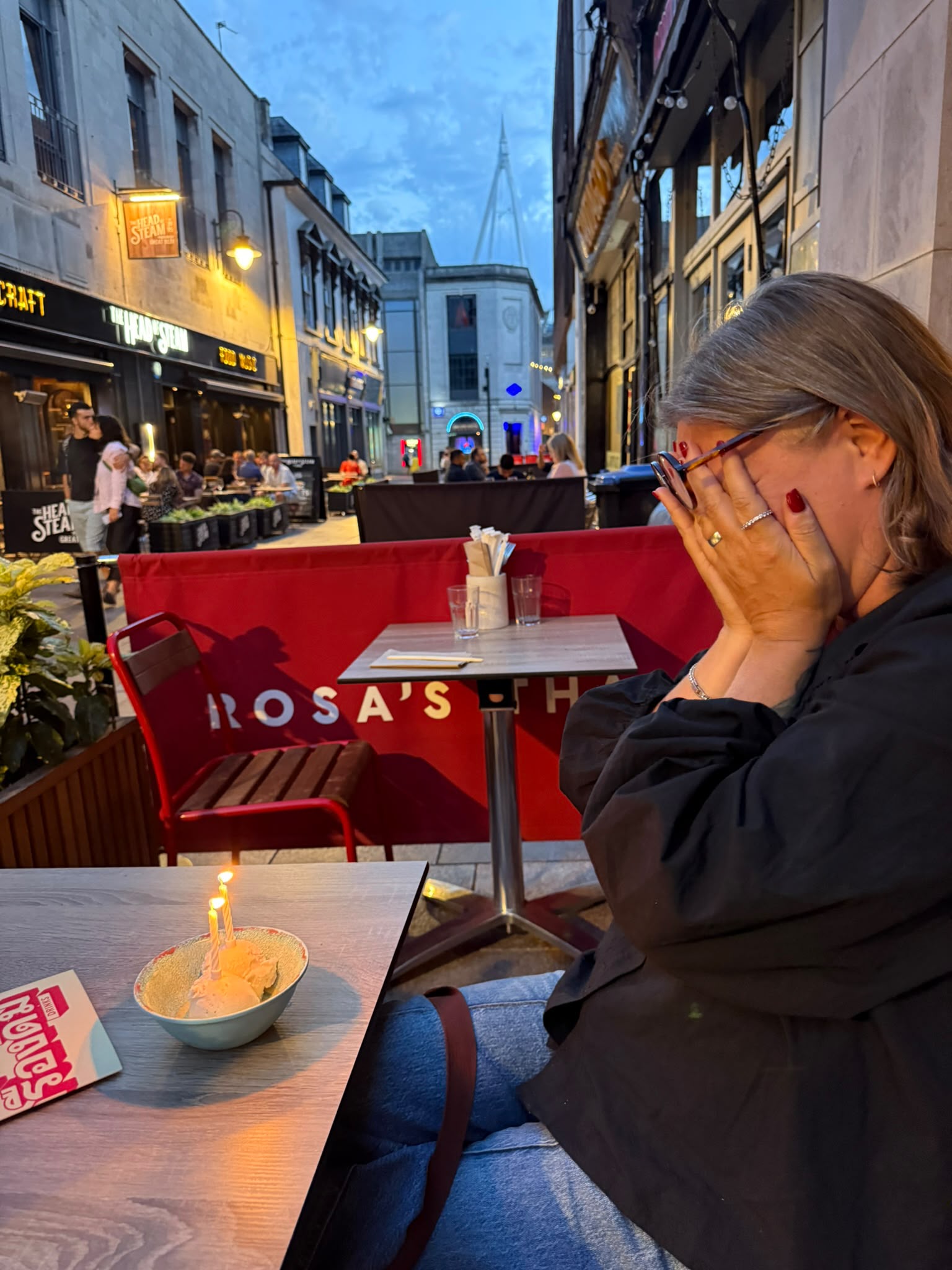 A birthday dessert with candles on an outdoor restaurant table at dusk