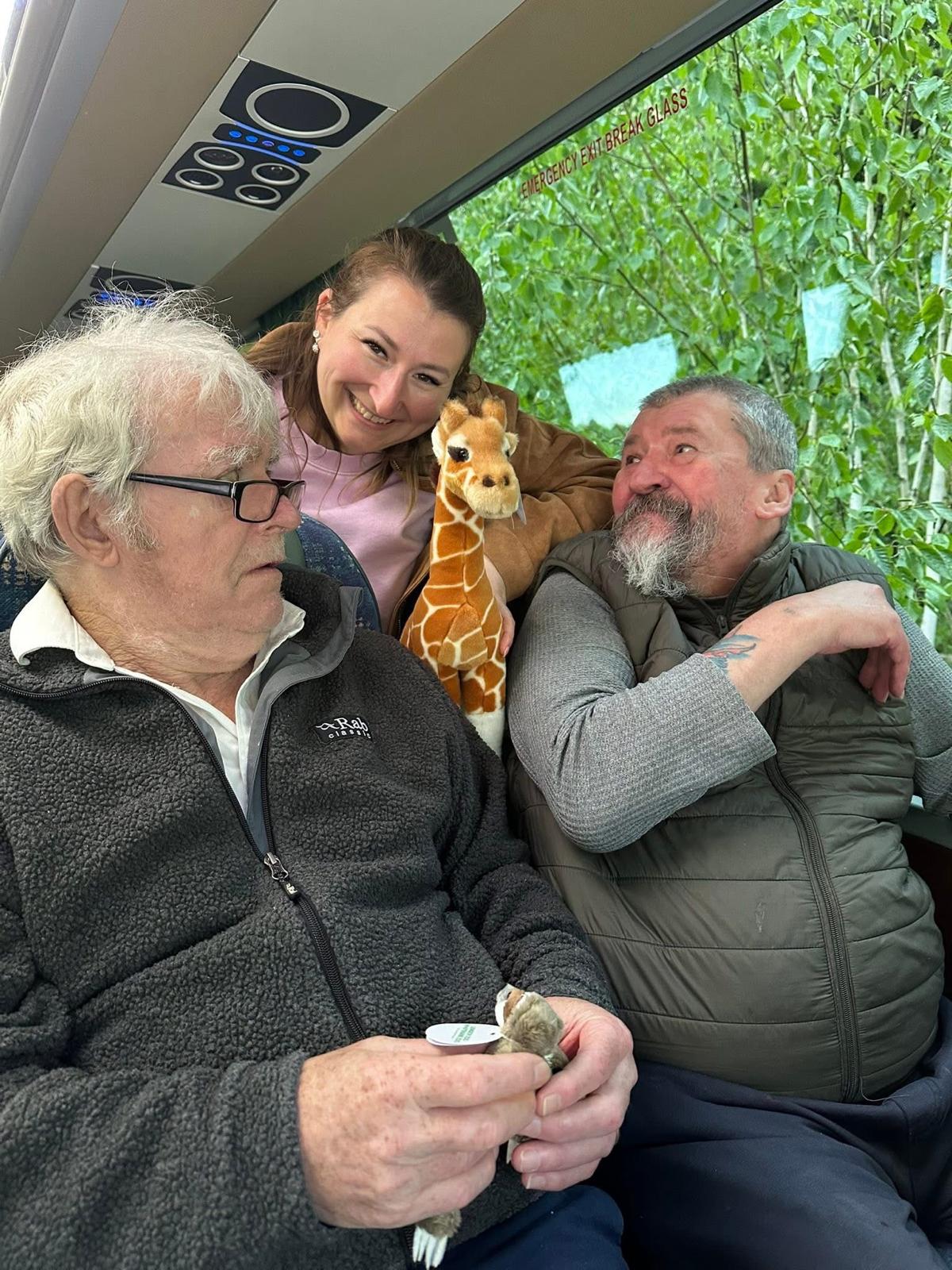 Friends sharing a laugh with a giraffe toy on board the coach
