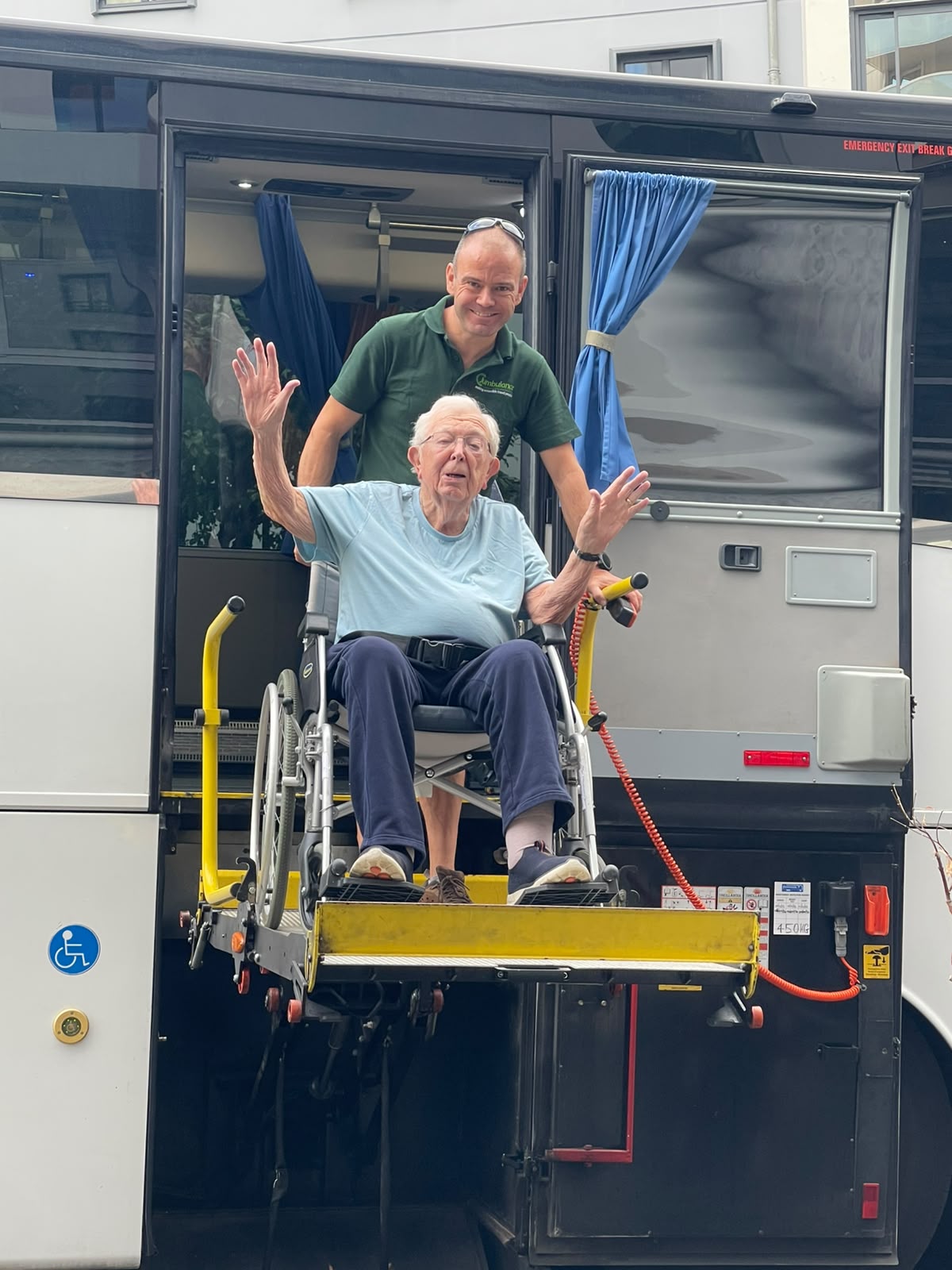 A passenger being helped onto a Jumbulance using the wheelchair lift, assisted by a driver.