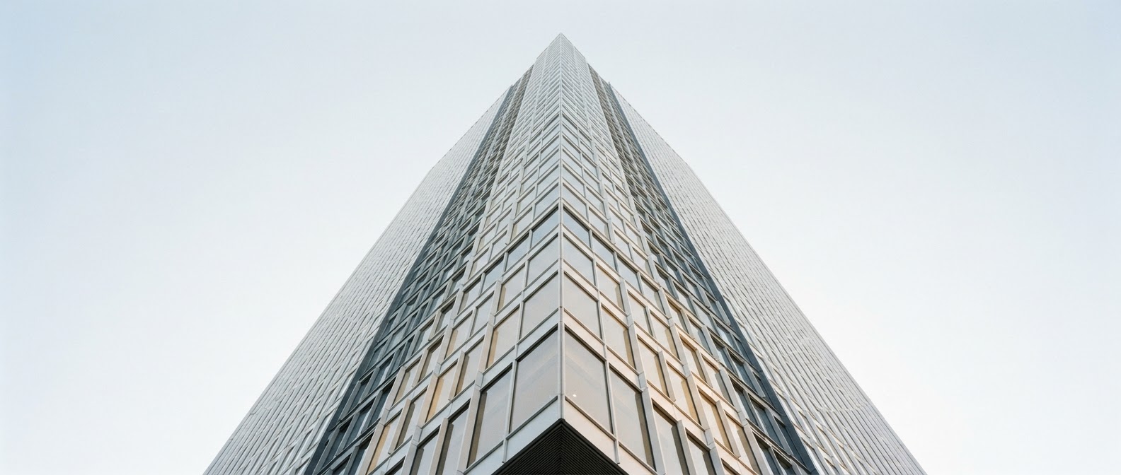 Looking up at the corner of a modern glass skyscraper against a clear morning sky
