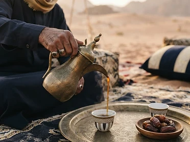 Arabic coffee poured from a dallah into a finjan on a brass tray