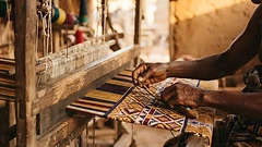 Ghanaian weaver hands threading kente cloth on a traditional loom