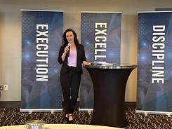 Kirstin Purcell speaking into a microphone in front of Execution, Excellence and Discipline banners