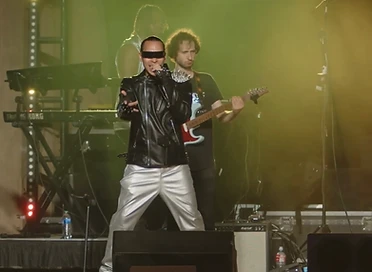 A lead vocalist gesturing in yellow-green stage haze, with a guitarist and a keyboardist performing behind.