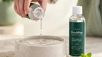 Capful of FreshPup liquid being poured into a dog water bowl