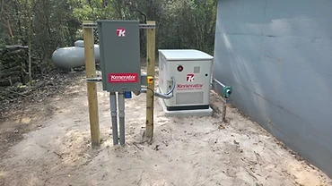 Kenerator generator and transfer switch box mounted on posts in a wooded backyard