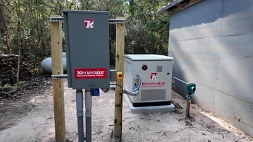 Kenerator generator installed on a concrete pad with its transfer switch box on wooden posts and a gas line connection