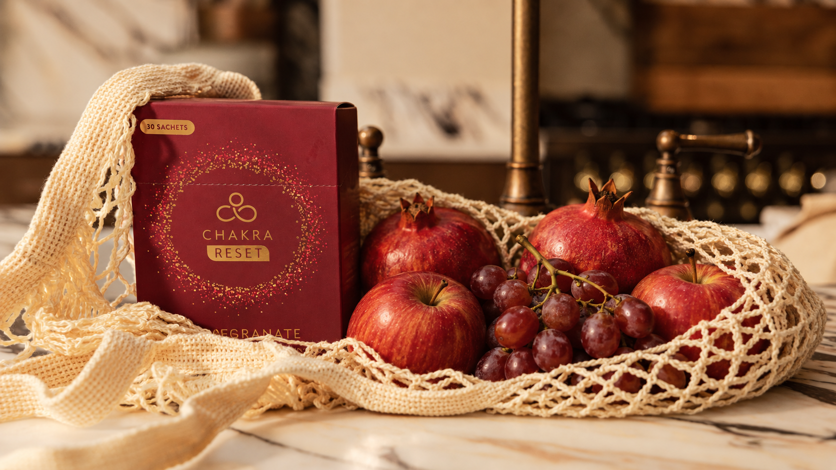 CHAKRA Reset pomegranate sachets with fresh pomegranates, apples and grapes in a woven mesh bag on a marble surface