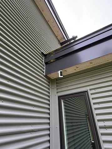 White wireless security camera mounted under a roof overhang on a corrugated metal building