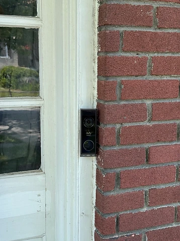 Eufy Security video doorbell mounted on a white door frame beside a red brick wall