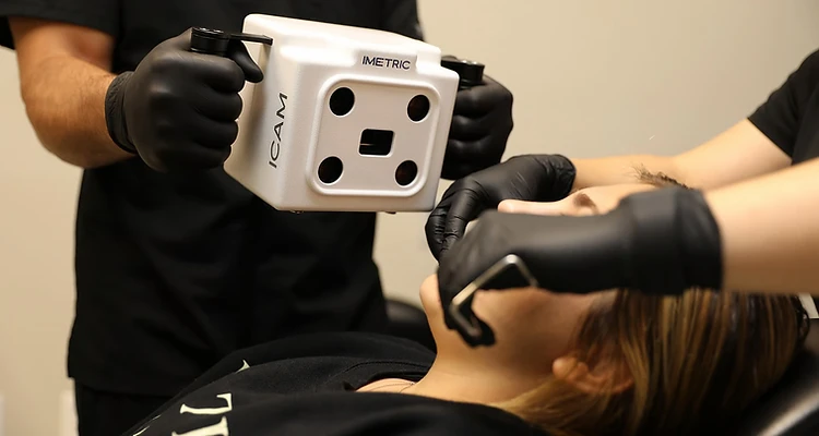 iCam4D scanner held by gloved hands above a patient during a clinical photogrammetry capture