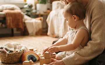 A parent and young child sharing play materials in soft natural light