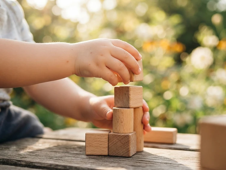 A child's small hands carefully stacking smooth wooden play blocks in warm morning light