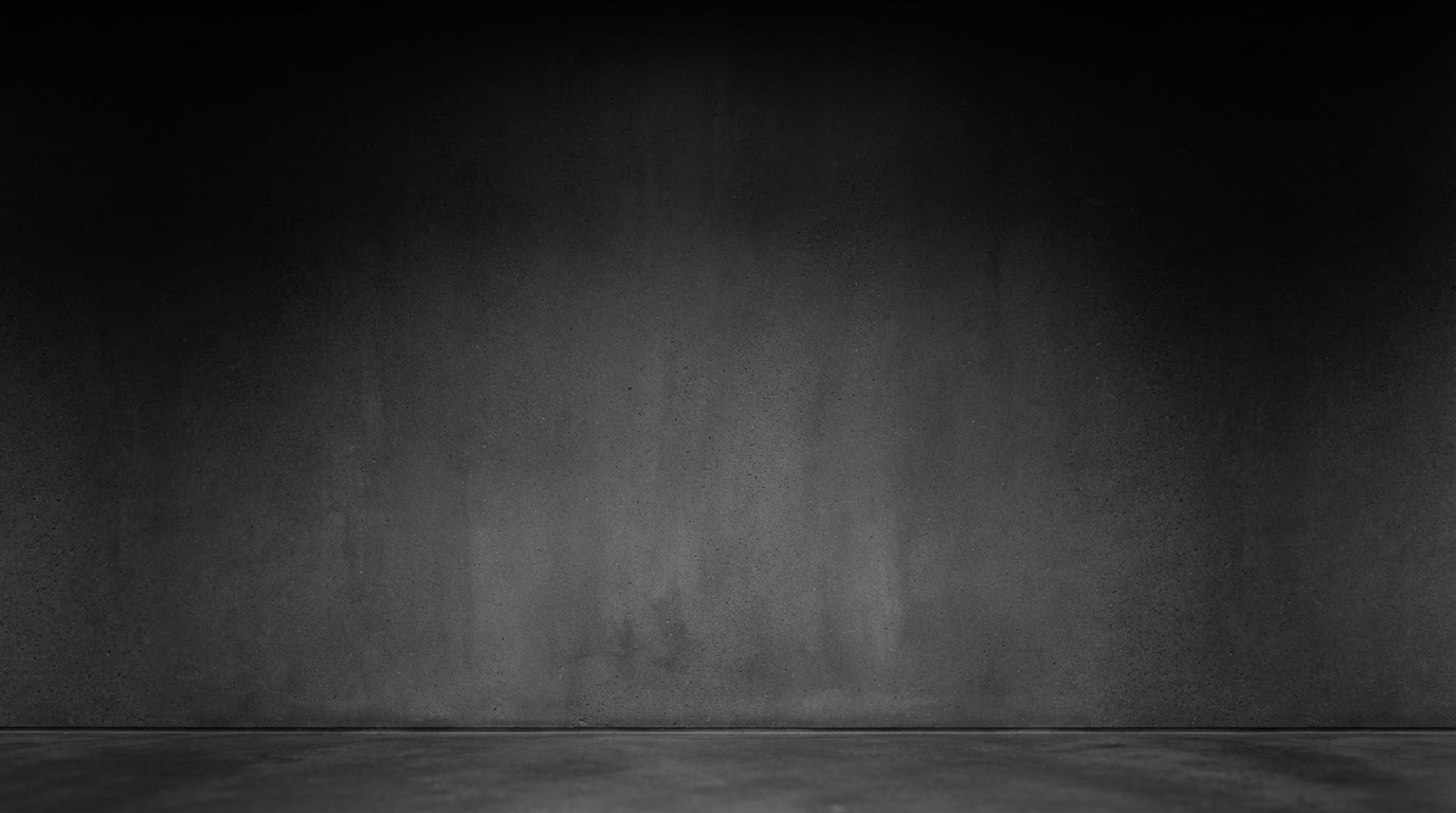 Minimalist empty room with grey textured walls, softly lit at the centre and fading into dark corners