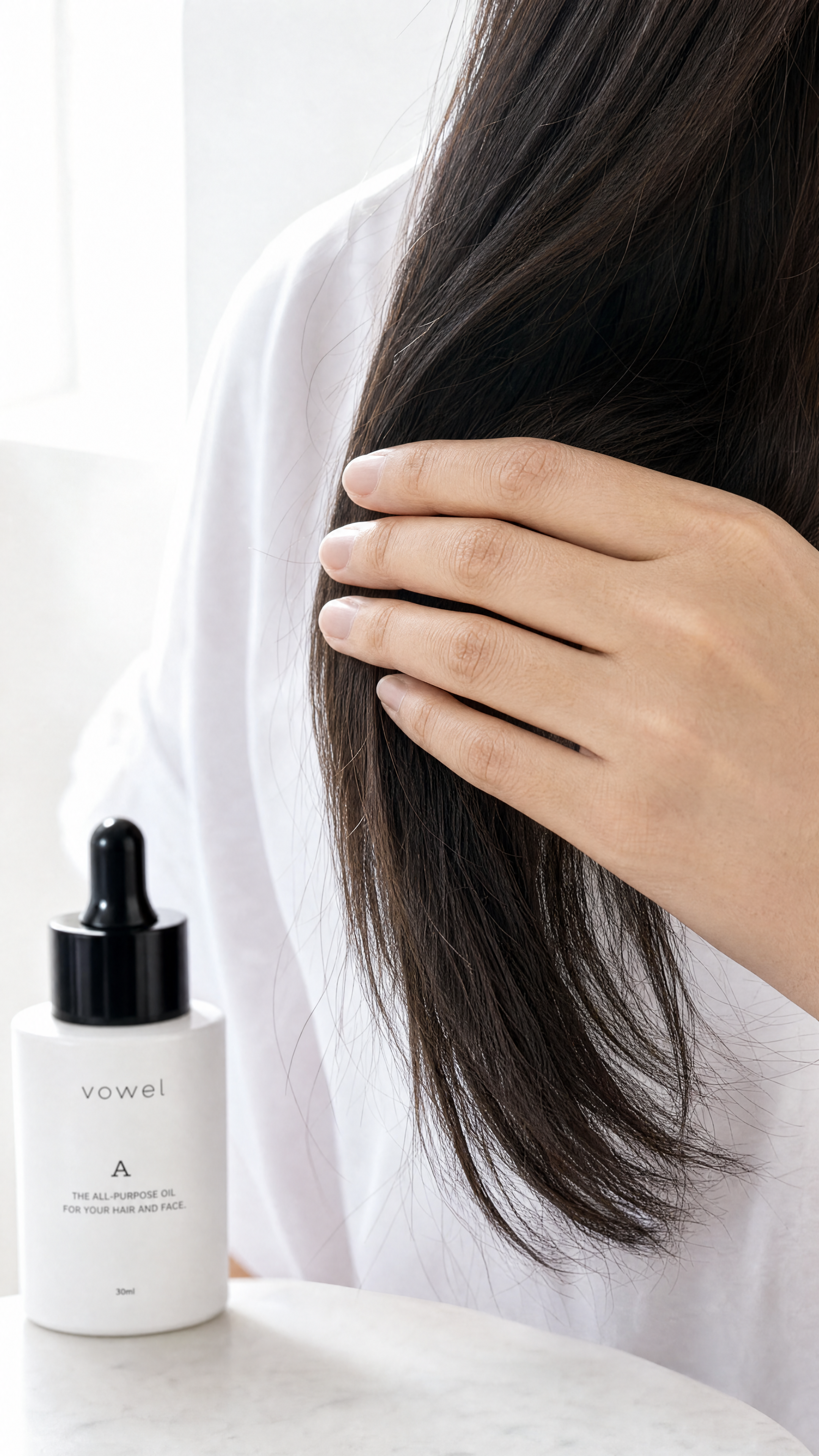 A hand stroking dark hair beside the vowel A bottle on a light marble surface