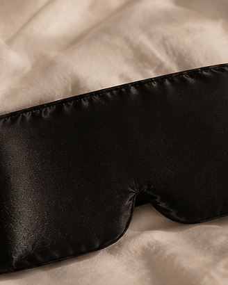 Masque de soie noir posé sur un lit en lin clair