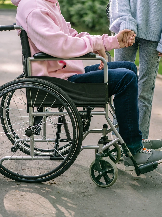 A Daybound companion warmly holding hands with a member seated in a wheelchair outdoors