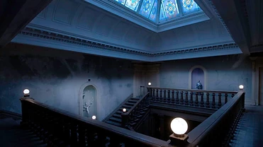 The dim stairwell atrium of a grand historic building at night beneath a stained-glass skylight